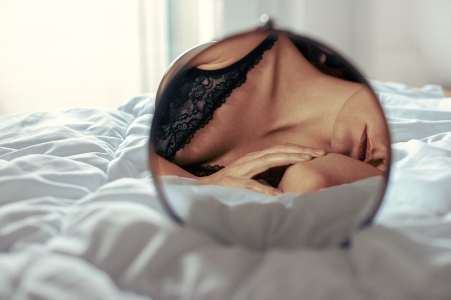 An Open Letter to Anyone Who's Been Told They're 'Too Sexual' - Woman relaxing at home on bed in the morning. Wearing lingerie and feeling confident and beautiful. Gently moving her fingers and touching her skin. Showing self love and daydreaming.