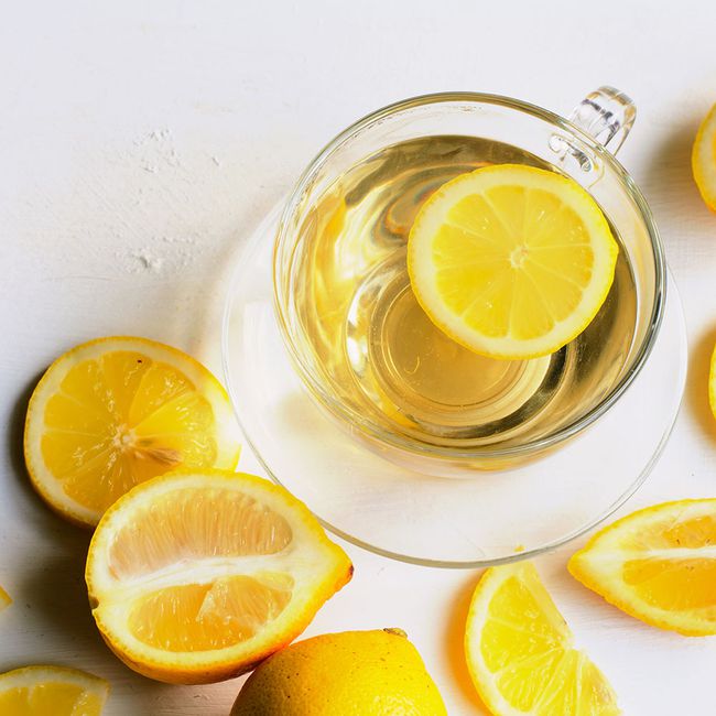 a glass mug filled with warm lemon water for bloating. various slices of lemon surround the bowl for decorative effect