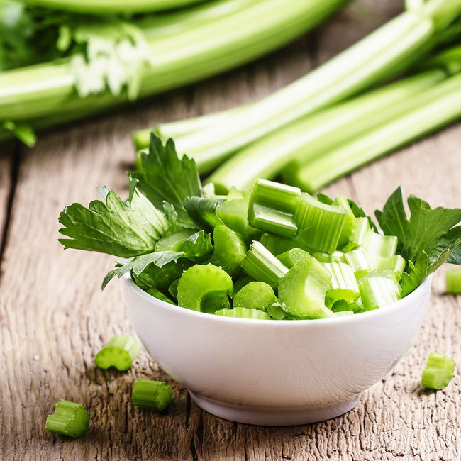 celery food to stop bloating: a white bowl filled with chunks of celery and celery leaves. celery stalks are seen in the background