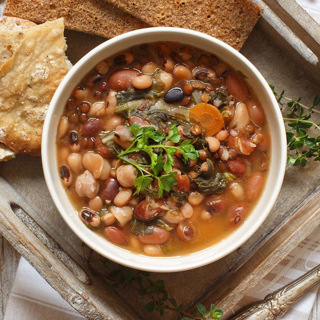 lentils and bean soup foods that help with bloating: a bowl of bean and lentil soup on a wooden serving tray, with slices of bread on the side