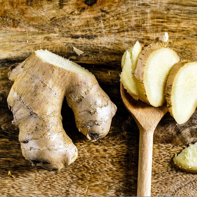 ginger food to help with bloating: on a wooden surface, half of a ginger root sits next to a wooden spoon with slices of the ginger root stacked on top of it
