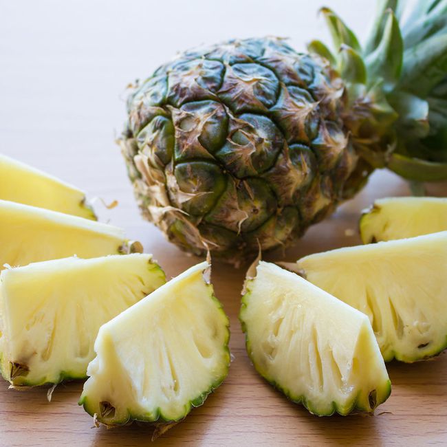 pineapple food to reduce bloat: a whole pineapple, lying on its side, is framed with seven pieces of sliced pineapple with rind
