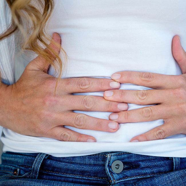 woman wearing white shirt and denim pants clutching stomach to indicate bloating and discomfort
