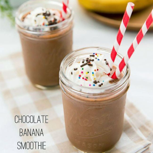 healthy banana smoothie recipes: two mason jars are filled with a chocolate banana smoothie, and each has two red-and-white striped paper straws, whipped cream, and chocolate and rainbow sprinkles as a garnish