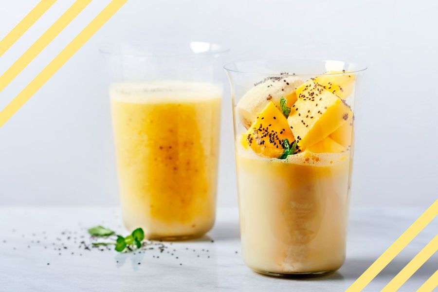 Two glasses of banana and mango smoothie on white background